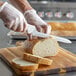 A person using a Mercer Culinary bread knife to slice a loaf of bread on a cutting board.
