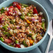A bowl of Furmano's cooked farro salad with tomatoes, onions, and cucumbers on a table.