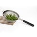 A OXO stainless steel mesh strainer with a black handle holding green beans.