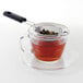 An OXO stainless steel strainer filled with tea sits on a glass cup.
