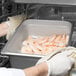 A person in gloves holding a Choice stainless steel steam table pan of shrimp.