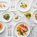 A table set with Acopa Liana bright white porcelain bowls filled with food and silverware.