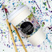 A white customizable coffee cup sleeve with a cup of coffee and paint brushes on a surface.