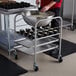 A man using a Vollrath Wear-Ever bun pan to prepare food on a metal cart.