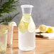 A Choice polycarbonate carafe of water with lemons and a glass on a table.