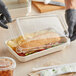 A gloved hand holding a plastic container with a sandwich and fries.