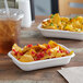 A white Eco-Products rectangle take-out container filled with nachos and a drink.