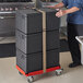A man pushing a stack of black Cambro Cam GoBoxes on a red Cambro Compact Camdolly.