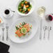 A plate of food with salmon, vegetables, and a lemon slice on an Acopa Edgeworth flatware set on a table.