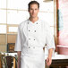 A man wearing a white Uncommon Chef 3/4 length sleeve chef coat standing in a professional kitchen.