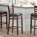 Three Lancaster Table & Seating mahogany wood ladder back bar stools with dark brown vinyl seats at a counter.