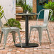 A black Lancaster Table & Seating outdoor table base on a table with gray chairs on a brick patio.