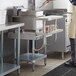 A man in a white apron using a Regency stainless steel equipment stand with shelves to cook in a commercial kitchen.