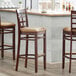 Three Lancaster Table & Seating mahogany wood bar stools with light brown vinyl window backs and seats at a bar counter.