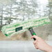 A hand using a Unger Monsoon Plus StripWasher with a green and white mop to clean a window.