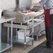 A woman using a Regency stainless steel equipment stand with a cutting board to cook in a commercial kitchen.