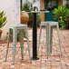 A Lancaster Table & Seating Excalibur bar height table base with two white stools on a brick patio.