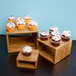 A set of three dark bamboo risers with cupcakes on them in a bakery display.