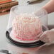 A person putting a cake with pink frosting in a plastic container with a clear dome lid.