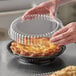 A person holding a plastic container over a pie.