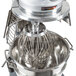 A Vollrath wire whisk attached to a mixer with a metal bowl.