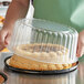 A person holding a Choice 8" cake in a plastic display container with a clear dome lid.