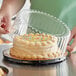 A person putting a frosted cake into a Choice plastic cake container with a clear dome lid.