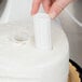 A hand using a white plastic Wilton cake pillar to cut a cake.