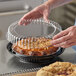 A person holding a black plastic container with a clear lid over a pie.