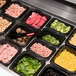 A black Araven plastic food pan with trays of sliced meat, corn, and green leaves.
