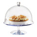 A Cal-Mil polycarbonate pedestal cake stand holding a pie under a glass dome on a table in a bakery.