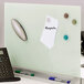 A Quartet white frameless glass dry erase desktop board with magnets and papers on it.