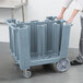 A person pushing a large grey Cambro dish caddy with a handle.