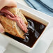 A hand dipping a sandwich into a bowl of Knorr Au Jus gravy.