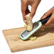 A person grating a ginger root with an OXO stainless steel grater.