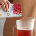 A hand pours Tazo Sweetened Passion Iced Tea Concentrate into a pitcher.