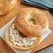 A sesame seed bagel with cream cheese on a wooden board.