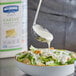 A bowl of salad being poured over with Hellmann's Caesar dressing.