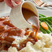 A person pouring Knorr brown gravy on a plate of meat and mashed potatoes.