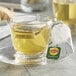 A glass cup of Lipton Classic Green Tea with a tea bag in it on a saucer.