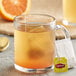 A glass mug of Lipton orange herbal tea with a tea bag in it.