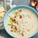 A bowl of Knorr Potato Chowder soup with bacon and green onions with crackers and a spoon.