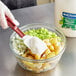 A gloved hand mixes Best Foods Vegan Mayonnaise into food in a bowl.