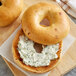 Two Original New York Style Sun Dried Tomato Bagels with cream cheese and herbs on a cutting board.