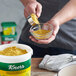 A person is mixing Knorr Caldo de Pollo yellow powder in a bowl.
