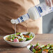 A person pouring Hellmann's Easy Pour Ranch Dressing from a white bottle onto a bowl of salad.