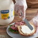 A person using a knife to spread Hellmann's Real Mayonnaise on a sandwich.