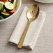 A gold slotted serving spoon on a white napkin next to a bowl of vegetables.