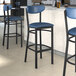 Three Lancaster Table & Seating Boomerang Series bar stools with navy vinyl seats and backs at a counter.