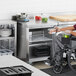 A man in a wheelchair using an Avantco ADA height worktop refrigerator to put food away in a black plastic tray.